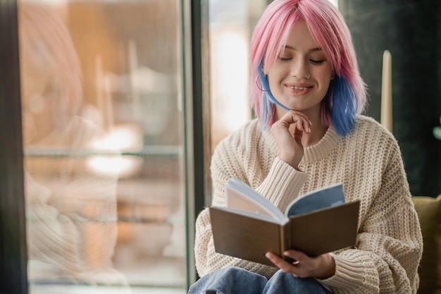 Leisure A girl with pink hair reading a book near the window