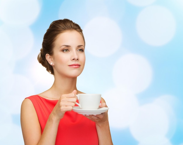 leisure, happiness and drink concept - smiling woman in red dress with cup of coffee over blue lights background