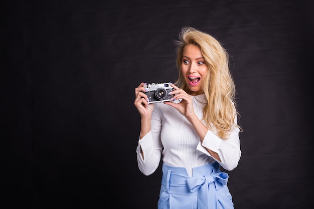 Leisure and hobby concept - Excited charming blonde woman with camera on black surface with copy space.