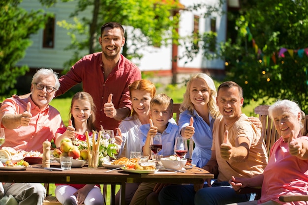 Photo leisure, holidays and people concept - happy family having festive dinner or summer garden party and showing thumbs up