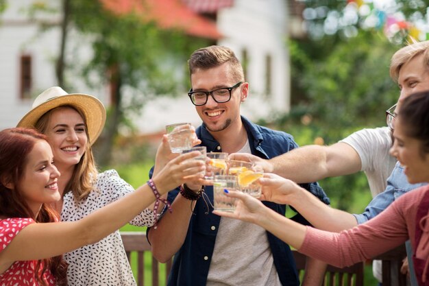 leisure, holidays, people, reunion and celebration concept - happy friends clinking glasses and celebrating at summer garden party