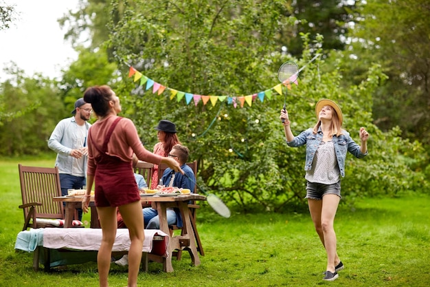 leisure, holidays, people and sport concept - happy friends playing badminton or shuttlecock at summer garden party