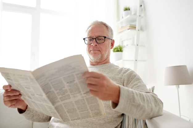 レジャー、情報、人々、マスメディアのコンセプト – 自宅で新聞を読む眼鏡をかけた年配の男性