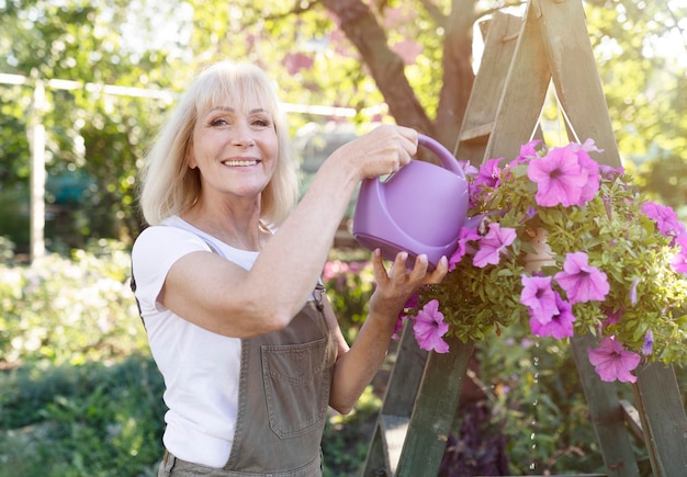 Concetto di stile di vita per il tempo libero donna matura felice che innaffia i fiori di petunia in vasi che fanno giardinaggio nel suo proprio