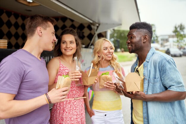 Photo leisure and people concept happy friends with drinks eating and talking at food truck