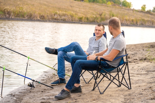 Leisure and people concept. Happy friends with fishing rods on pier by lakeside.