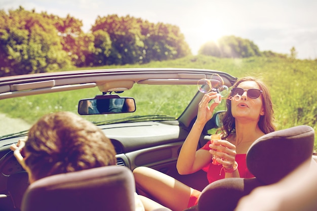 Foto concetto di tempo libero, viaggio su strada, viaggio e persone - amici felici che guidano in auto cabriolet lungo la strada di campagna e soffiano bolle