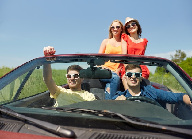 leisure, road trip, travel and people concept - happy friends driving in cabriolet car along country road