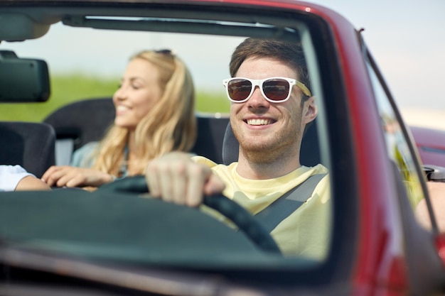 leisure, road trip, travel and people concept - happy friends driving in cabriolet car along country road