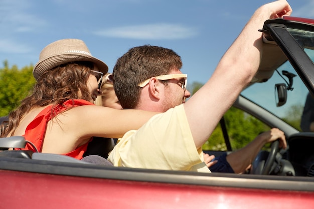 Photo leisure, road trip, travel and people concept - happy friends driving in cabriolet car along country road