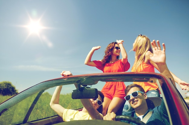 Concetto di tempo libero, viaggio su strada, viaggio e persone - amici felici che guidano in auto cabriolet lungo la strada di campagna