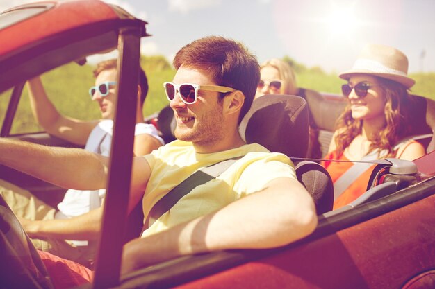 leisure, road trip, travel and people concept - happy friends driving in cabriolet car along country road