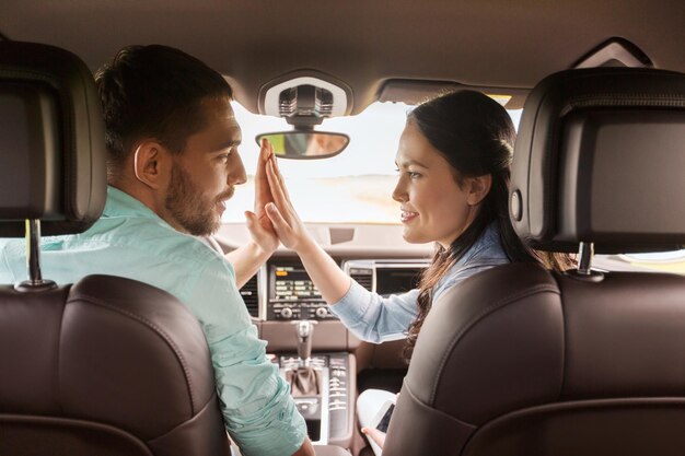 leisure, road trip, travel and people concept - happy man and woman making high five gesture and driving in car