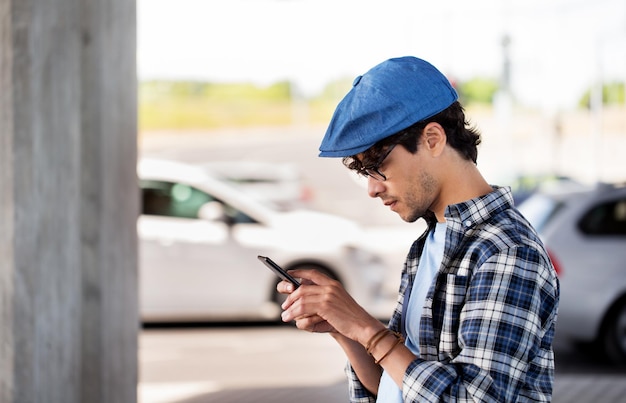 leisure, technology, communication and people concept - hipster man texting message on smartphone on city street