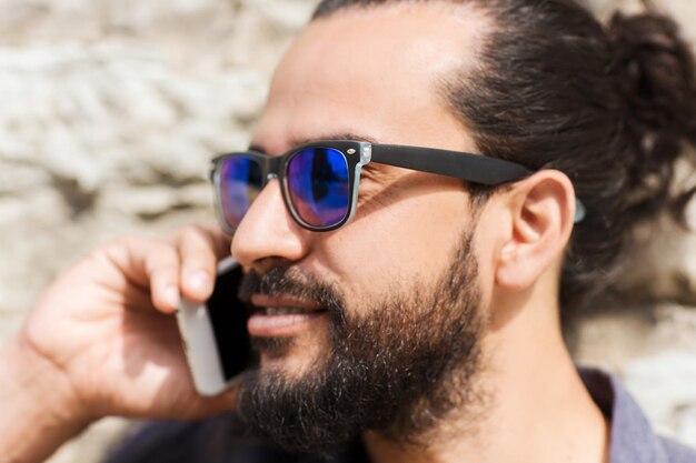 leisure, technology, communication and people concept - man calling on smartphone on street at stone wall