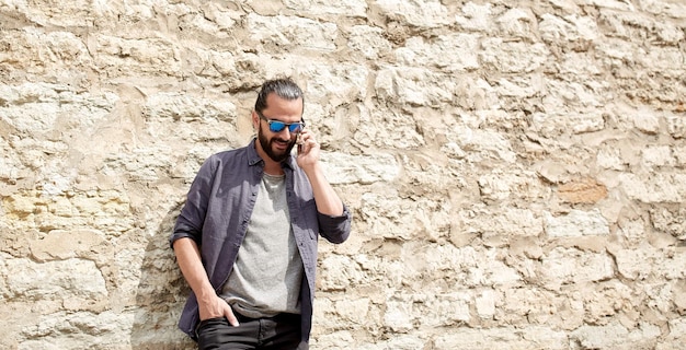 leisure, technology, communication and people concept - smiling man calling on smartphone at stone wall on city street