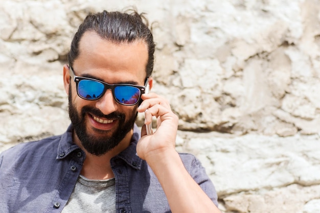 leisure, technology, communication and people concept - smiling man calling on smartphone on street at stone wall