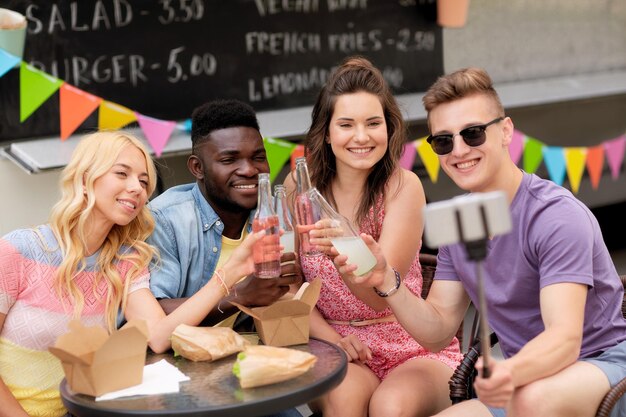 Photo leisure technology and people concept happy young friends with food and drinks and taking selfie at food truck