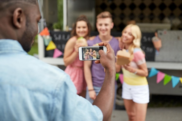 Photo leisure technology and people concept young man taking picture of his happy friends eating hamburgers and wok at food truck