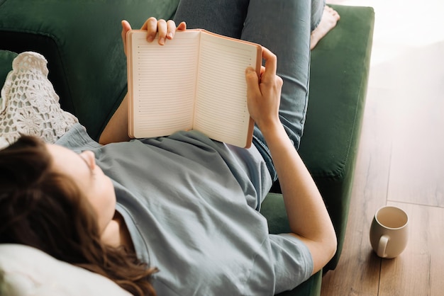 Leisure Time Young Woman Enjoying Book Meal and Tea on Living Room Sofa Relaxed Reading and Dini