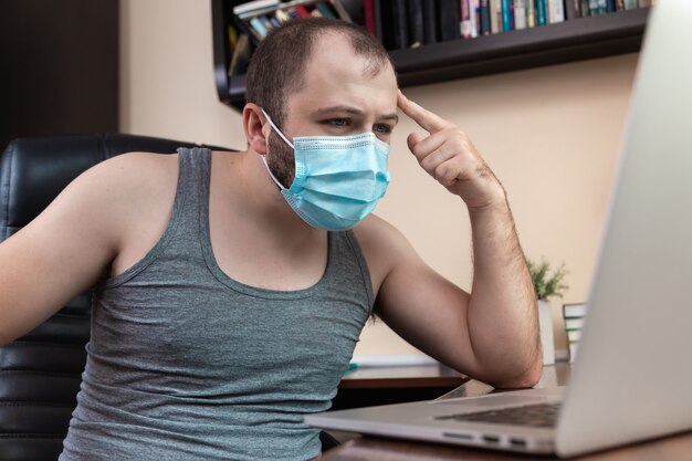 Photo leisure using laptop. a young bearded guy with face mask in home clothes uses laptop