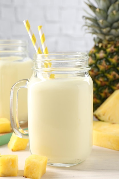 Lekker ananas smoothie in een pot en vers fruit op een witte houten tafel.
