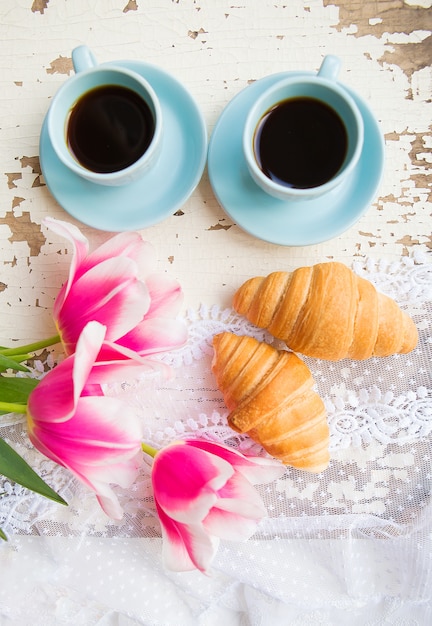 Lekker kopje koffie, croissants en roze tulpen op oude witte tafel