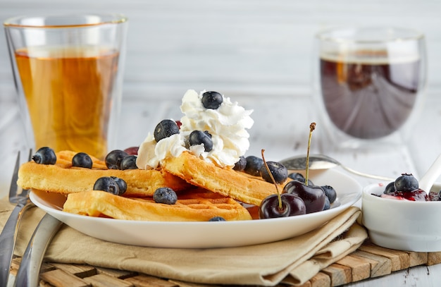 Lekker ontbijt. Belgische wafels met slagroom bosbessen en jam op een houten wit