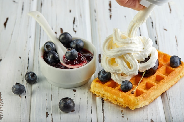 Lekker ontbijt. Belgische wafels met slagroom bosbessen en jam op een houten wit