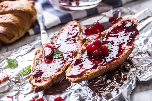 Lekker ontbijt met rode aalbessen marmelade croissants boter en muntblaadjes.