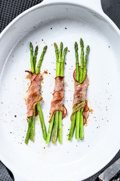 Lekker varkensvlees spek rond asperges in een ovenschaal.