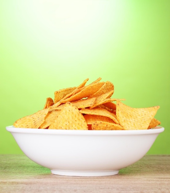 Lekkere aardappelchips in witte kom op houten tafel op groene achtergrond