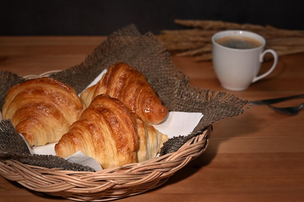 Lekkere boterachtige croissants in rieten mand en koffiekopje op houten tafel