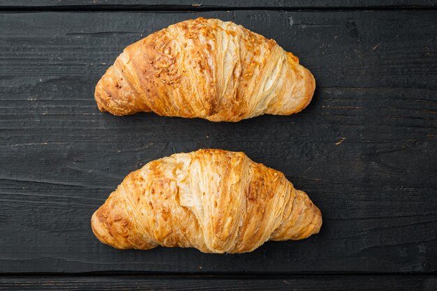 Lekkere boterachtige croissants set, op zwarte houten tafel achtergrond, bovenaanzicht plat lag