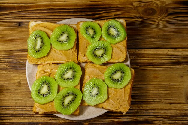 Lekkere broodjes met pindakaas en kiwi's op houten tafel top view