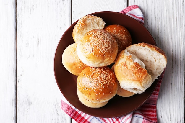 Lekkere broodjes met sesam op plaat op een houten achtergrond kleur