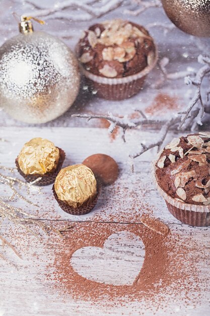 Lekkere chocolade cupcake met snoep, hartvormige cacaopoeder en winterdecoratie op witte rustieke houten tafel. Winter vakantie achtergrond.