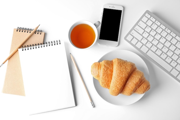 Lekkere croissant kopje thee smartphone en notebooks op witte achtergrond