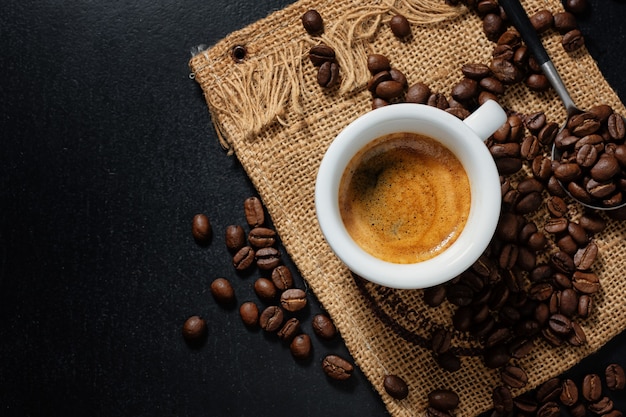 Lekkere dampende espresso in beker met koffiebonen. Uitzicht van boven. Donkere achtergrond.