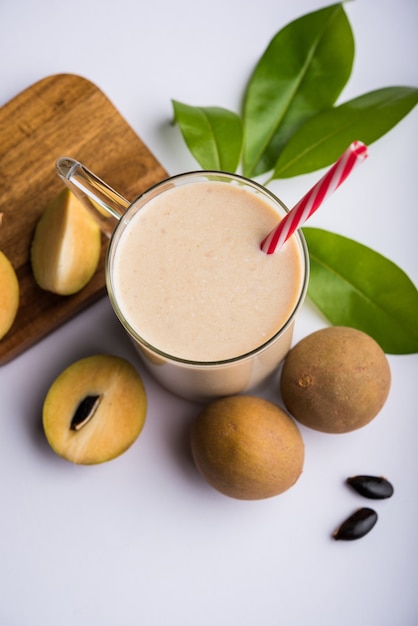 Lekkere en gezonde Chickoo, Chikoo OF Sapota Milkshake. Het is een gezond fruit gemengd met melk en ijs geserveerd in een glas op een kleurrijke of houten achtergrond. Selectieve focus