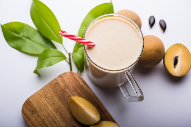 Lekkere en gezonde chickoo, chikoo of sapota milkshake. het is een gezond fruit gemengd met melk en ijs geserveerd in een glas op een kleurrijke of houten achtergrond. selectieve focus