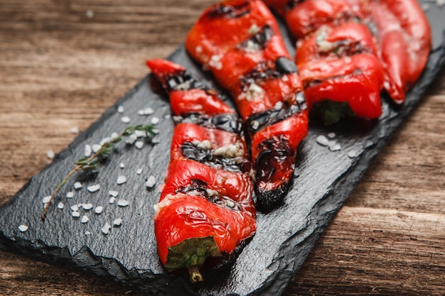 Lekkere en sappige gegrilde chilipeper geserveerd op zwarte slade, close-up weergave.