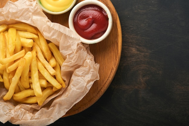 Lekkere frietjes server op perkamentpapier op houten snijplank met tomaat en kaassaus op houten tafel achtergrond Diverse Keto gerechten Fast food en ongezond voedsel concept