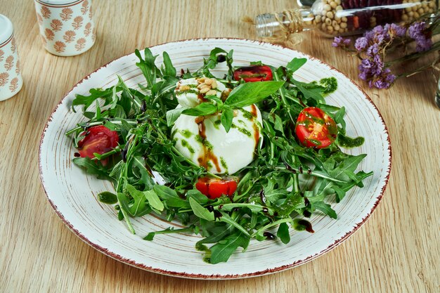 Lekkere, frisse salade met mozzarella burrata, rucola, cherrytomaatjes en basilicum op een grijze plaat op een houten tafel. zachte Italiaanse kaasburrata. Italiaanse keuken. Detailopname