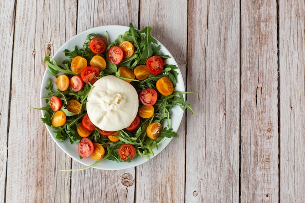 Lekkere, frisse salade met mozzarella burrata, rucola, cherrytomaatjes en basilicum op een witte plaat