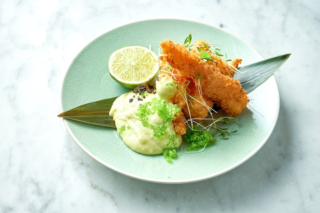 Lekkere garnalenfrietjes, gepaneerd met witte saus, groene tobiko kaviaar en limoen gearchiveerd in een groene plaat op een marmeren tafel. garnalen in aziatische stijl. restaurant zeevruchten