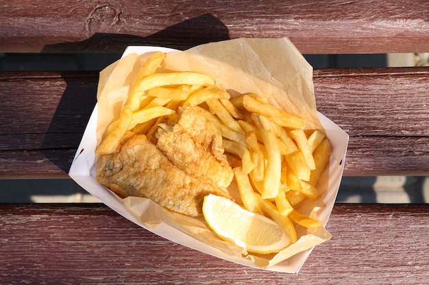Lekkere gebakken fish and chips met schijfje citroen op houten ondergrond