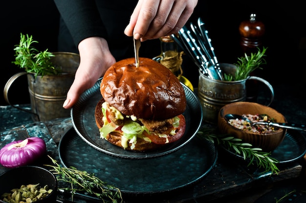 Lekkere gegrilde zelfgemaakte hamburgers met kippengehakt, tomaten en uien In de handen op een zwarte achtergrond