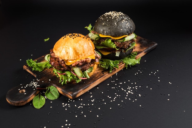 Lekkere hamburgers met zwart-wit broodje op houten bureau op de zwarte achtergrond
