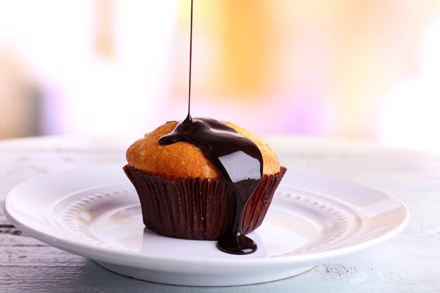 Lekkere muffin met chocoladesaus op plaat op lichte achtergrond